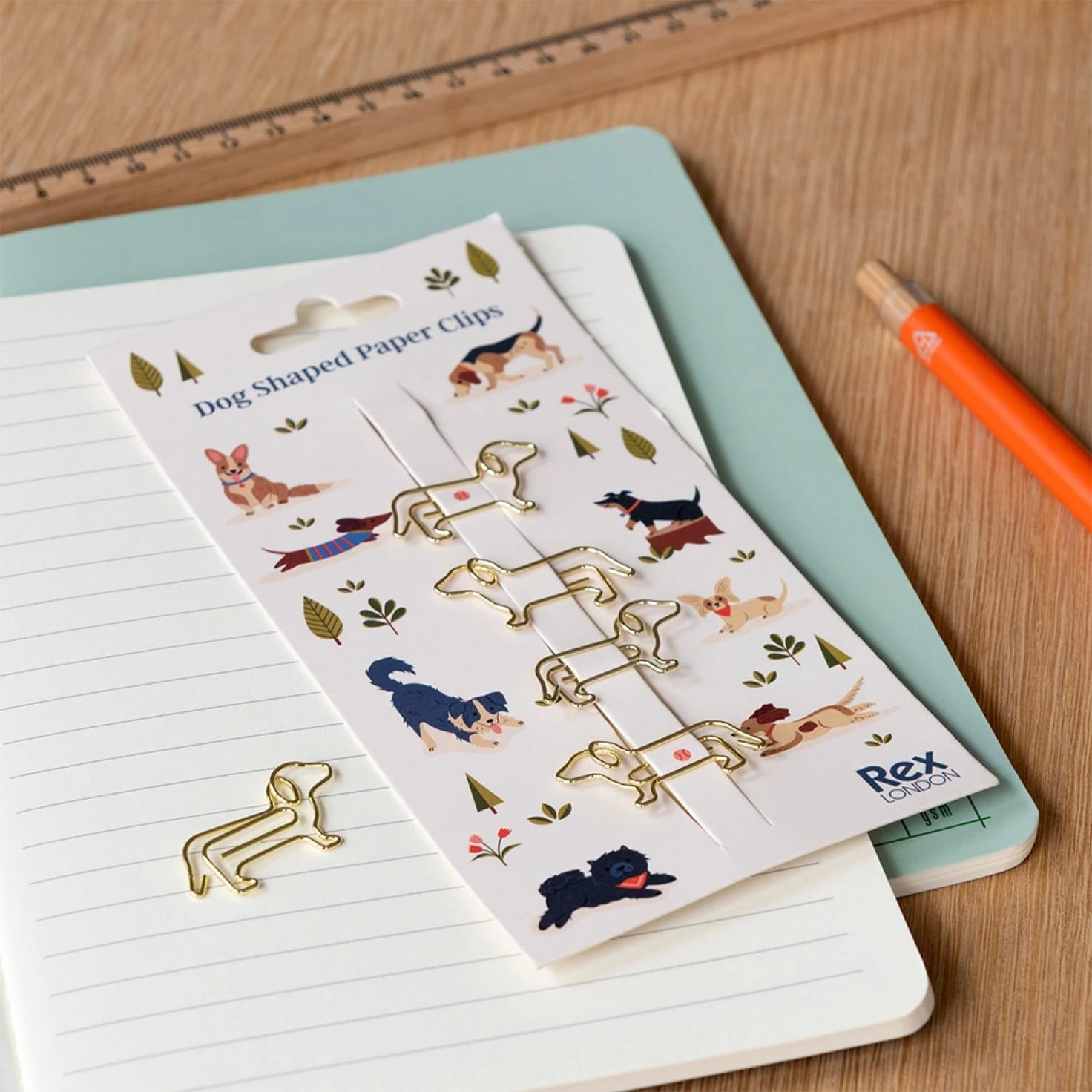 Clips de papel dourados em forma de cão em cartão ilustrado sobre cadernos numa mesa de madeira
