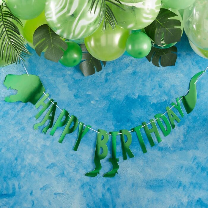 Decoração de festa com balões verdes, folhas artificiais e pendente de dinossauro com texto Happy Birthday