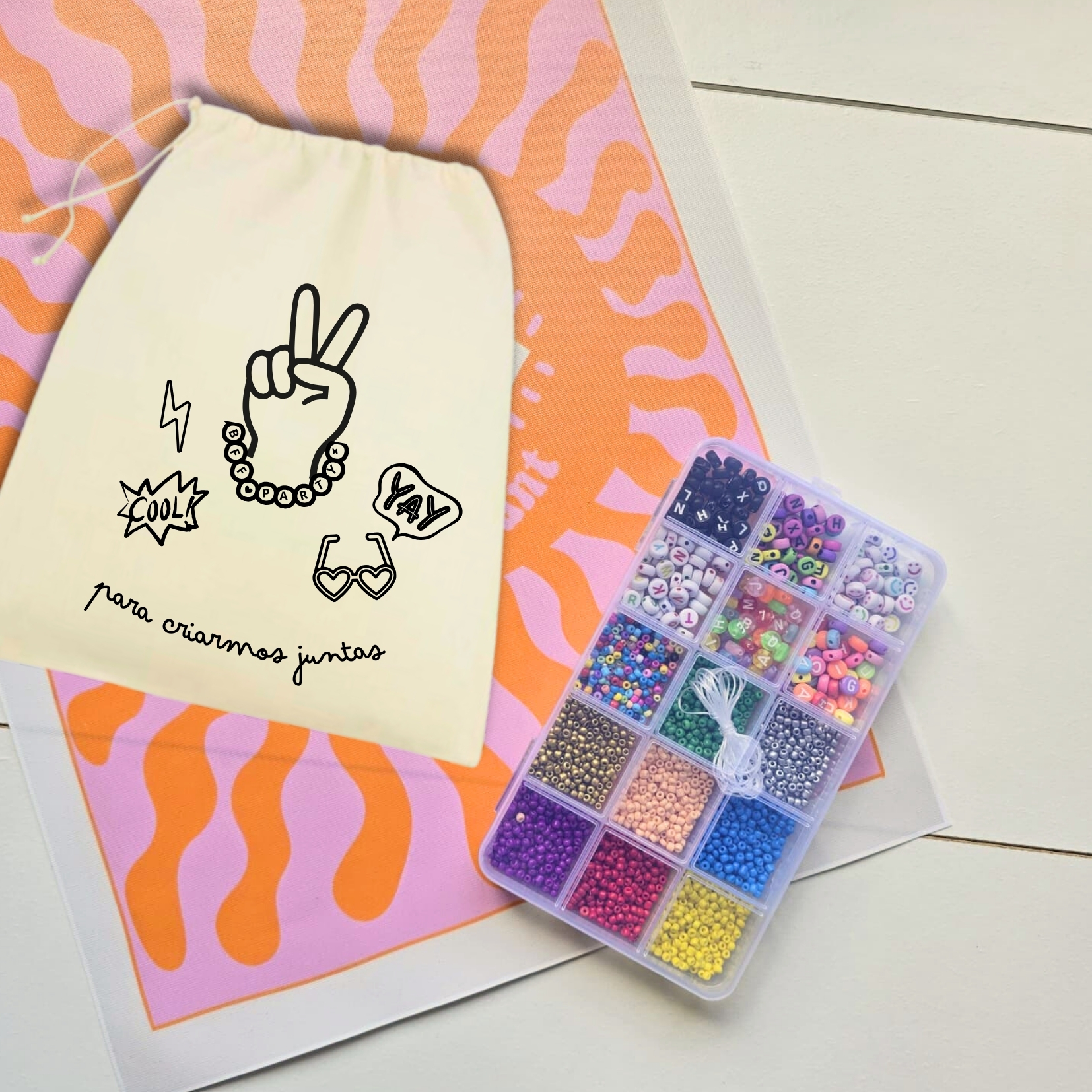 Saco de algodão com desenho preto e caixa de miçangas coloridas em fundo rosa e laranja