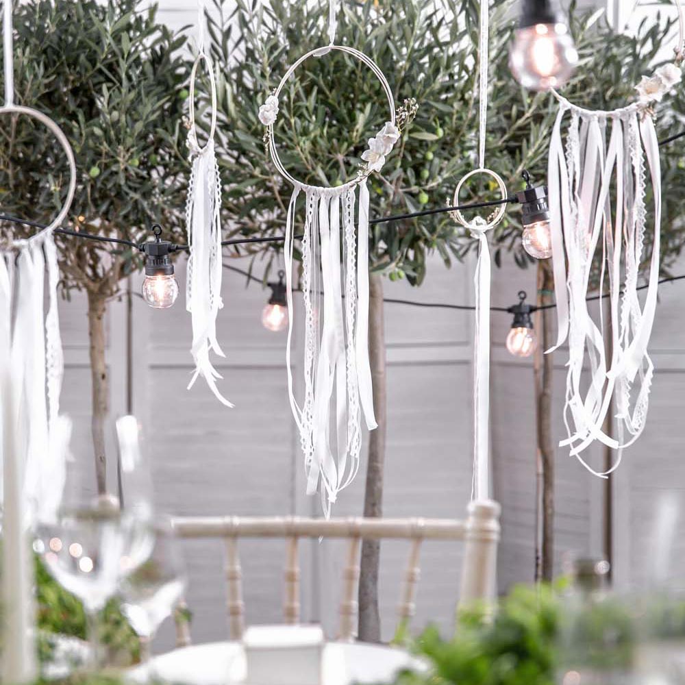 Três apanhadores de sonhos brancos pendurados entre árvores e luzes de cordão