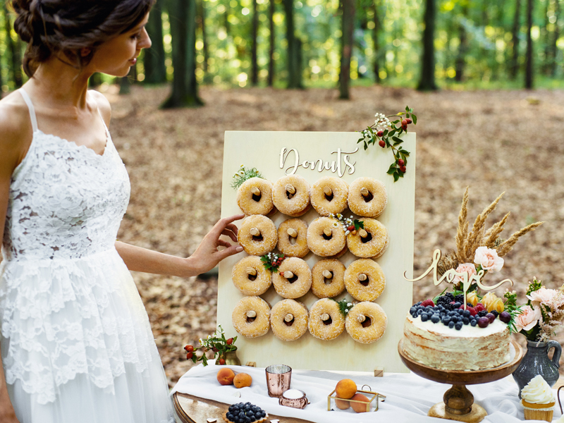 Painel de donuts decorado e bolo com frutos sobre mesa em floresta