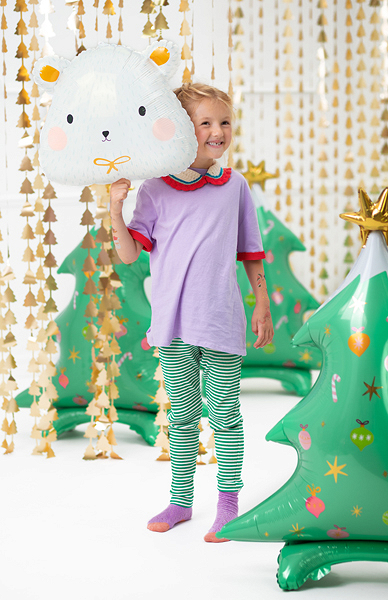 Criança com balão de urso e vestido colorido com árvores de Natal insufláveis ao fundo