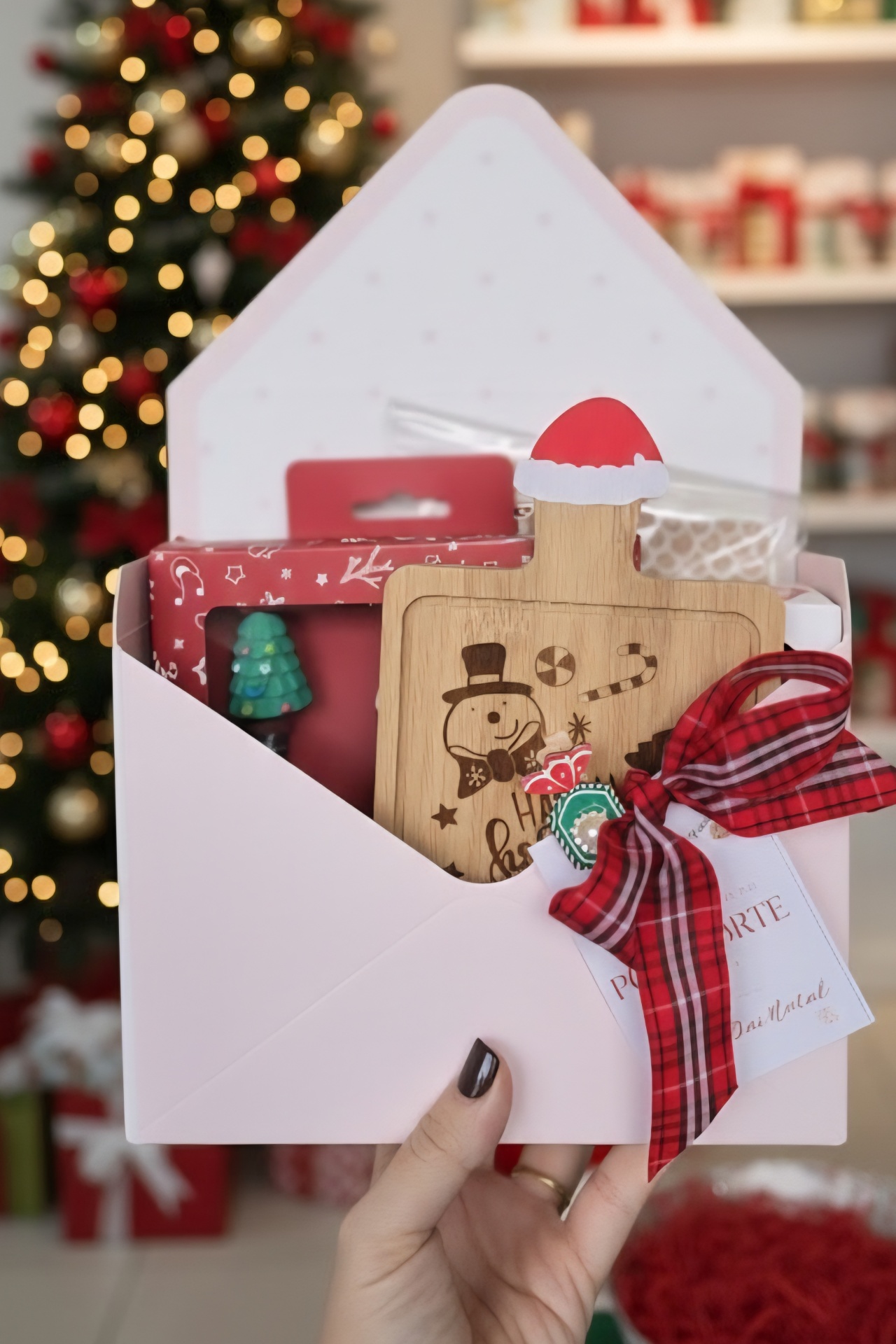 Conjunto de presente de Natal com tábua de madeira decorada, fita vermelha e caixa branca em envelope.