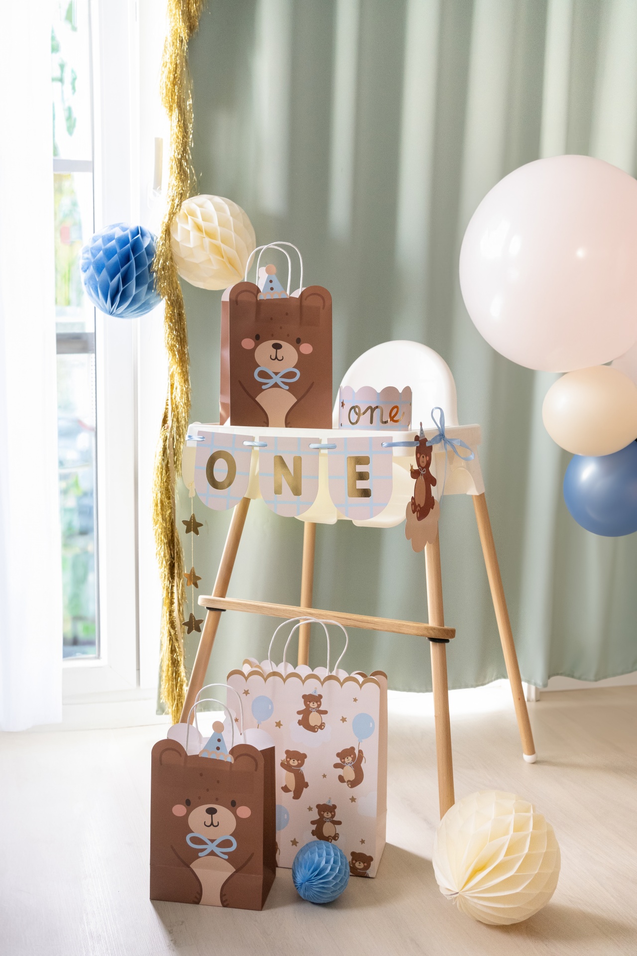 Cadeira alta branca decorada para festa de aniversário com sacos de urso, balões e faixa com palavra ONE.