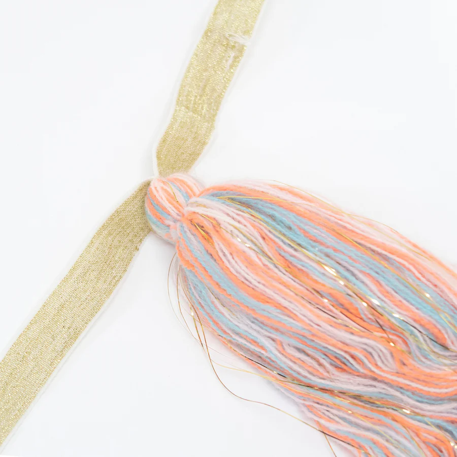 Pendente decorativo em fios coloridos pastel com fios metálicos, pendurado numa fita bege.