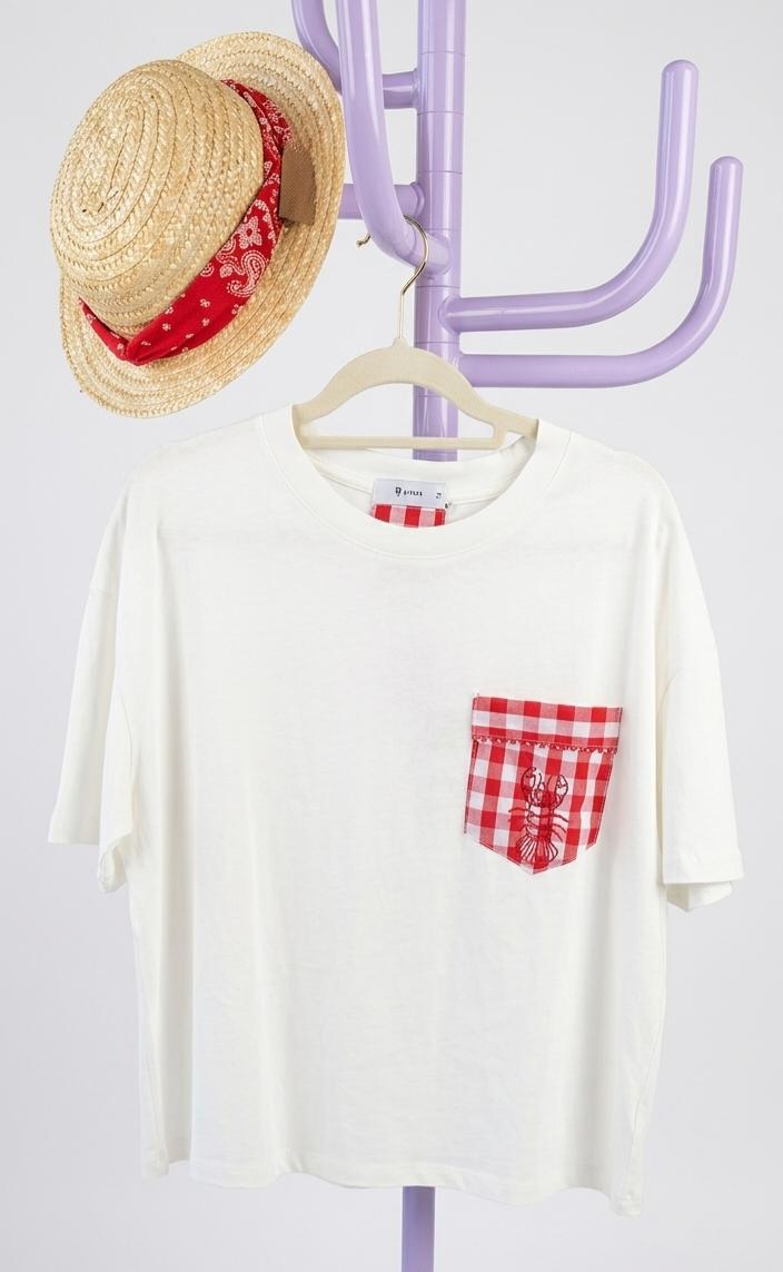 T-shirt branca com bolso xadrez vermelho e branco e chapéu de palha com lenço vermelho pendurados num porta-chapéus lilás