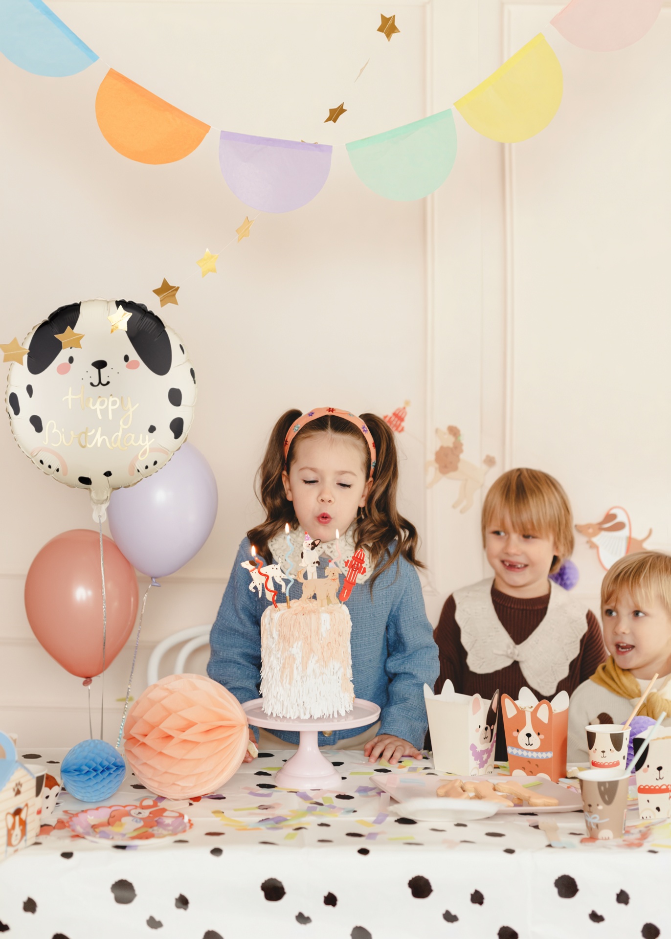 Festa de aniversário infantil com decoração colorida, bolo, balões e crianças à mesa.