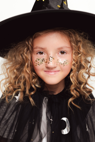 Criança com chapéu de bruxa preto e capa preta com purpurinas douradas no rosto