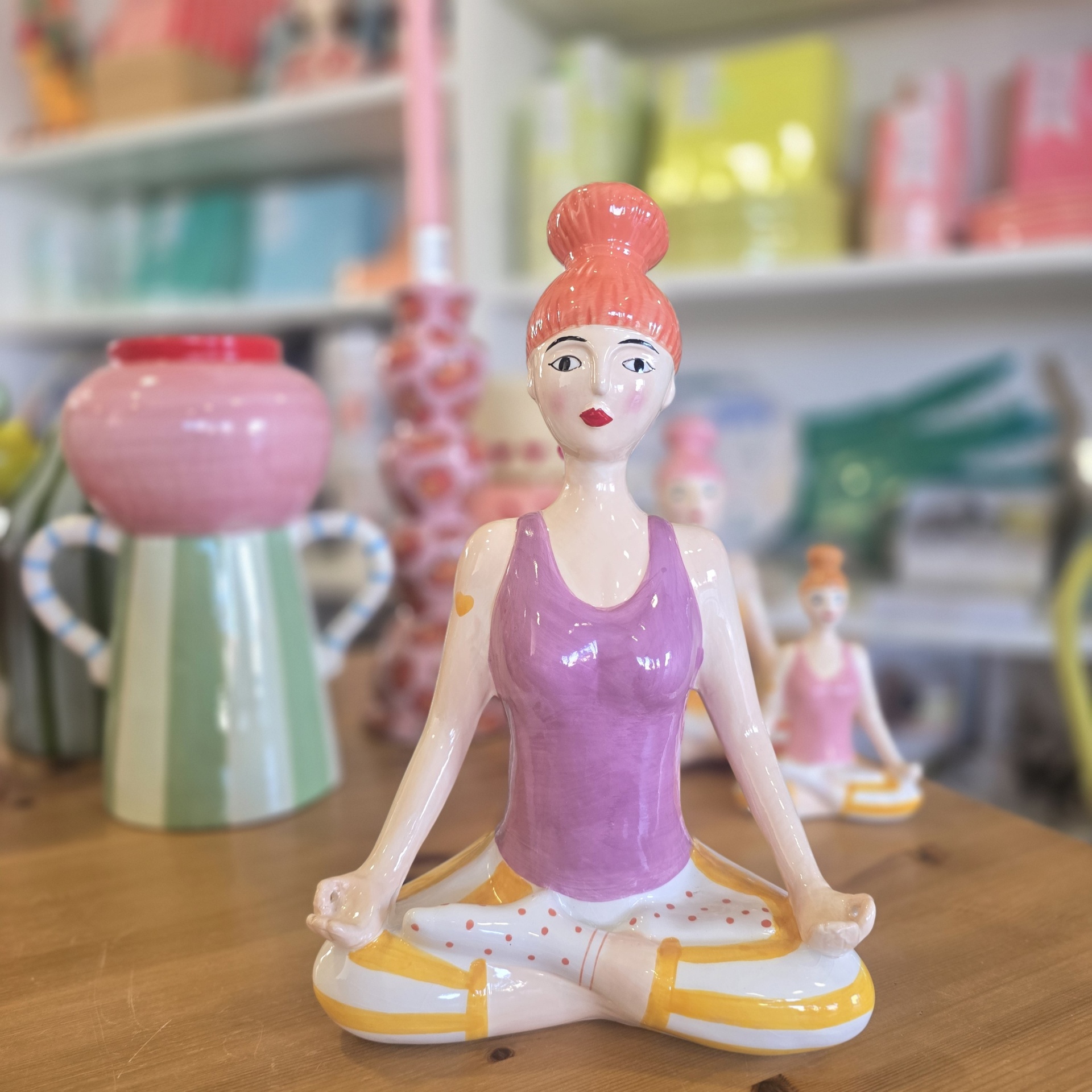 Estátua de cerâmica decorativa de mulher meditando com top roxo e calças brancas com padrão.