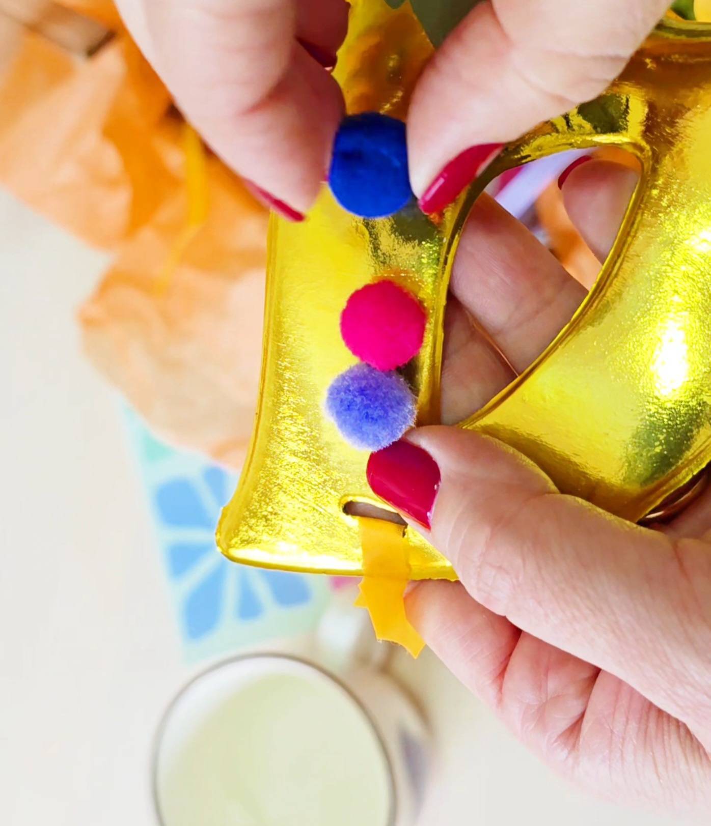Mãos segurando objeto dourado em forma de letra com pompons coloridos