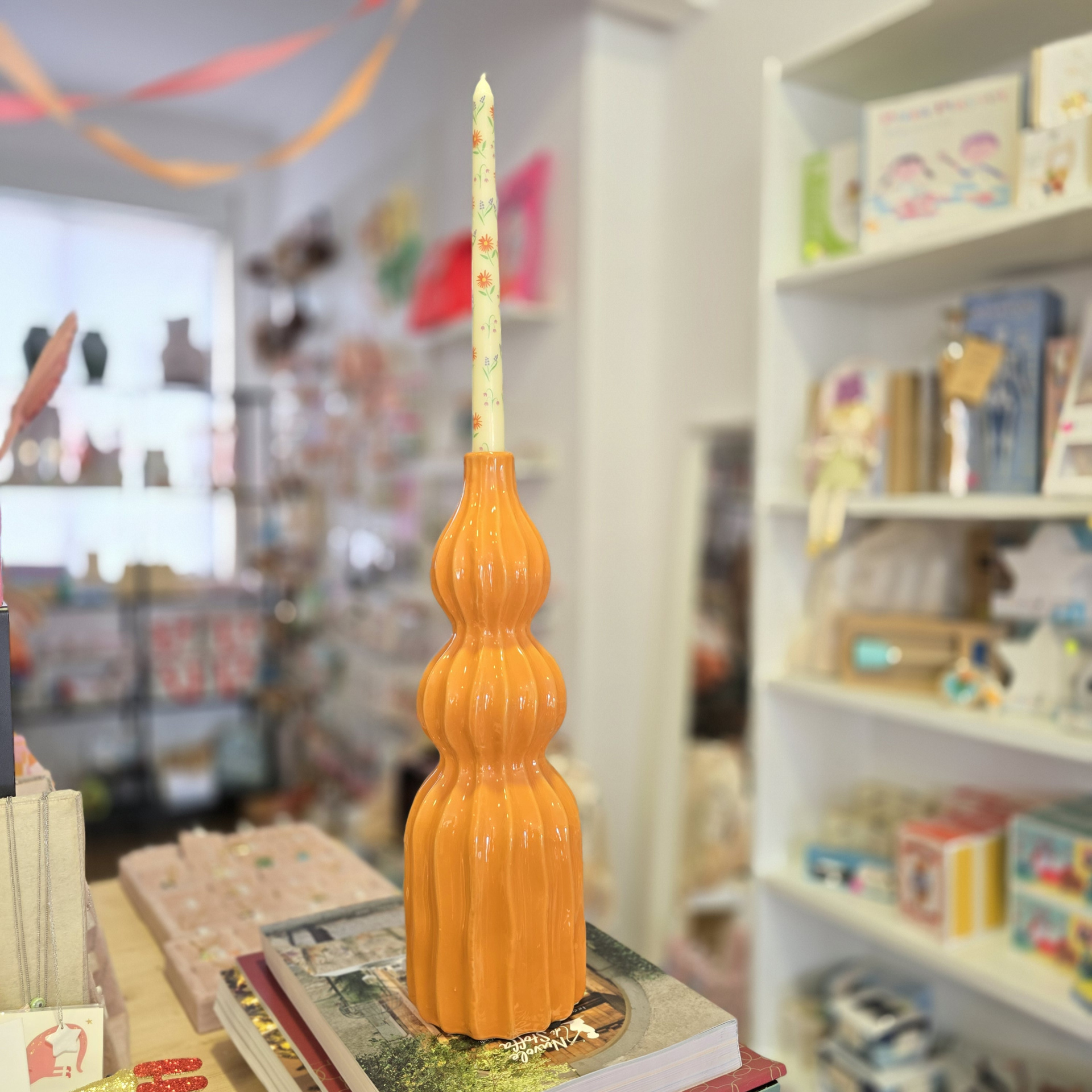 Vela decorativa com padrão floral em suporte de cerâmica laranja sobre livros