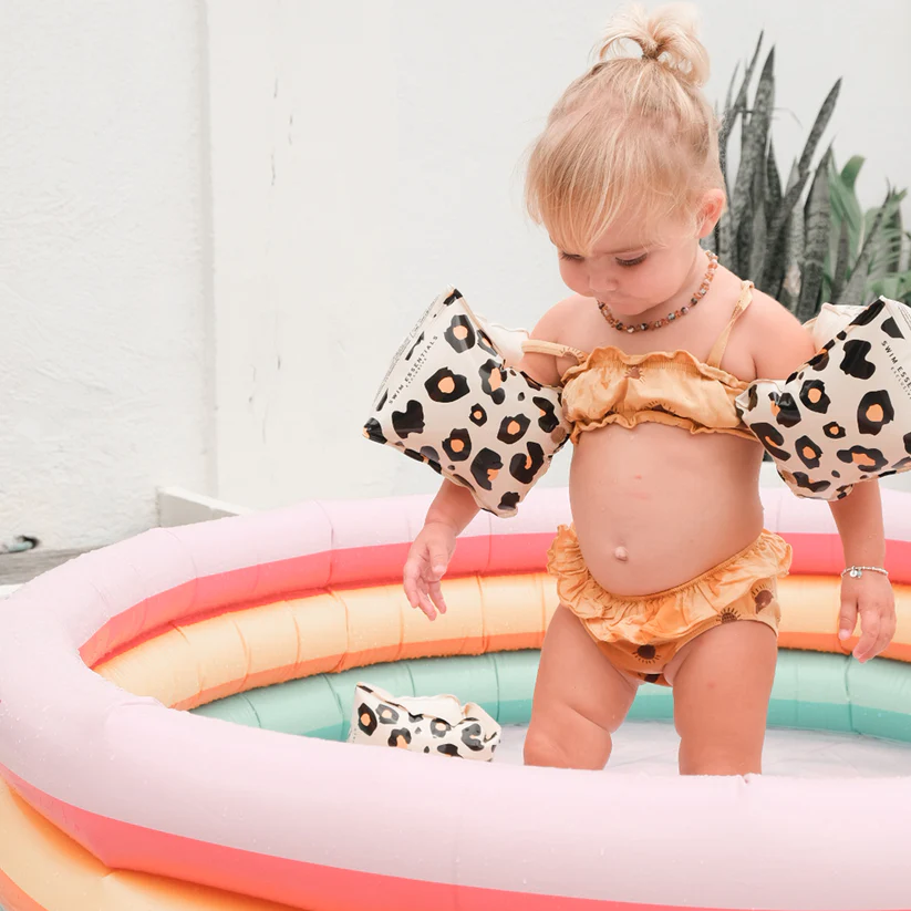 Criança com fato de banho laranja e braçadeiras animal print em piscina insuflável colorida