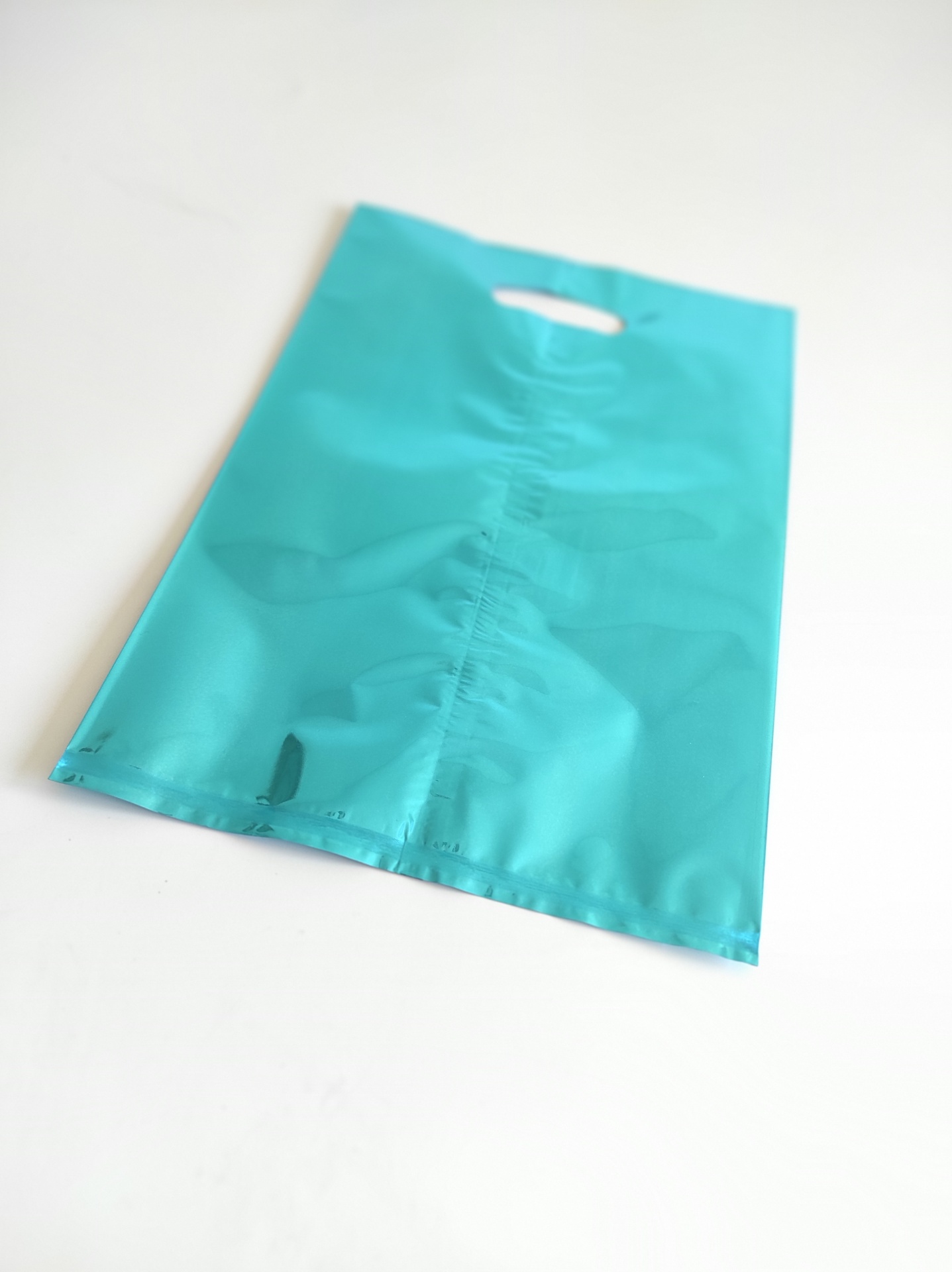 Saco plástico azul turquesa com pega, sobre fundo branco