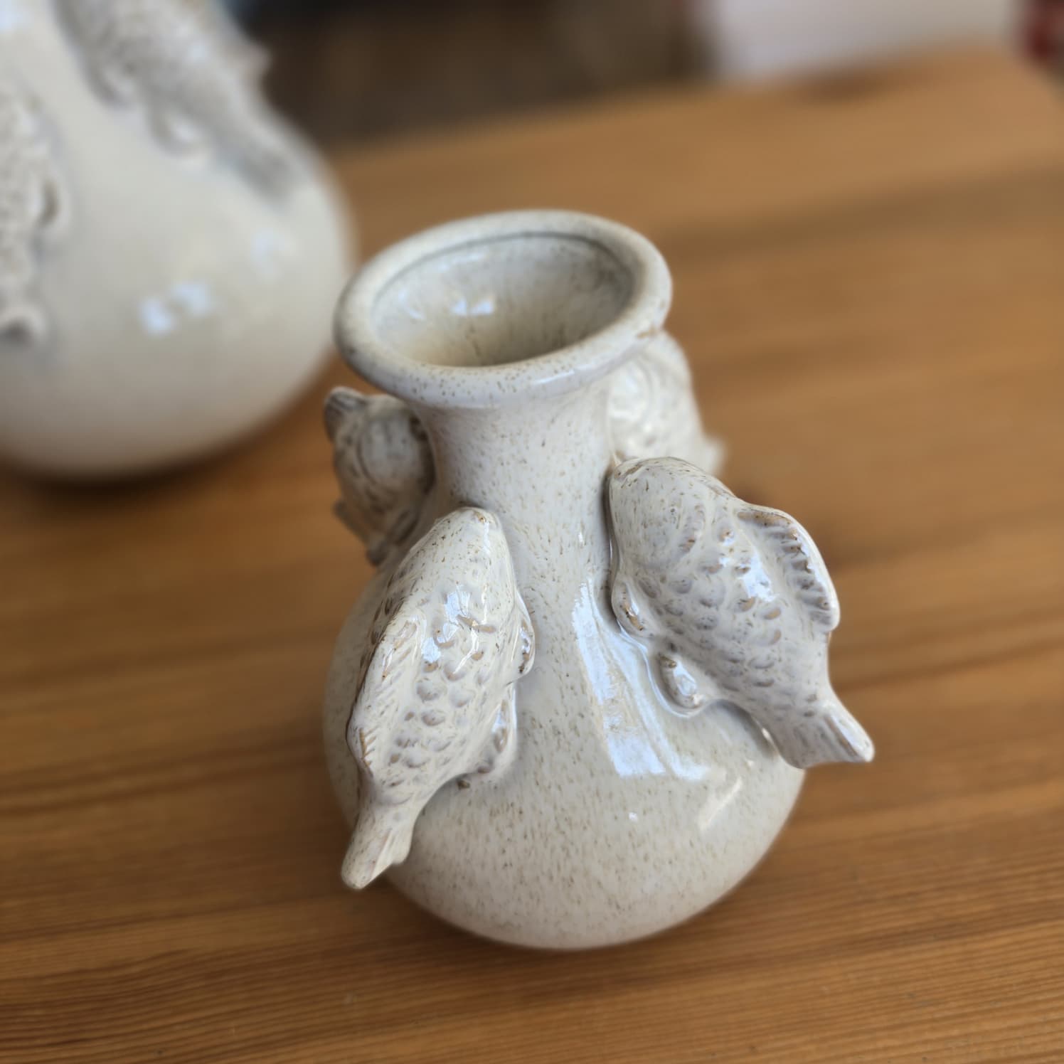 Vaso cerâmico creme com peixes em relevo sobre mesa de madeira