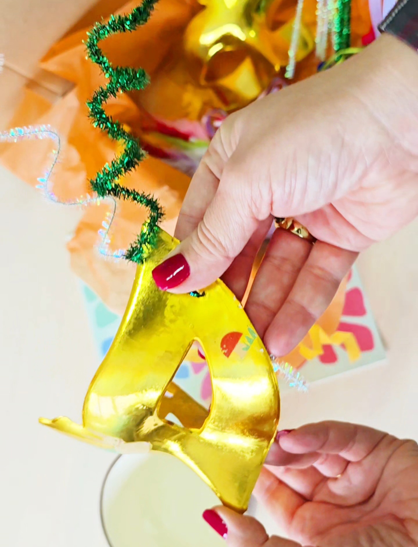 Diadema dourada em forma do número 4 com decoração espiral segurada por mãos femininas