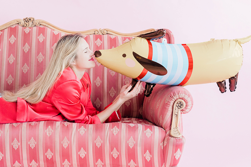 Mulher com pijama vermelho no sofá rosa a beijar balão em forma de cão