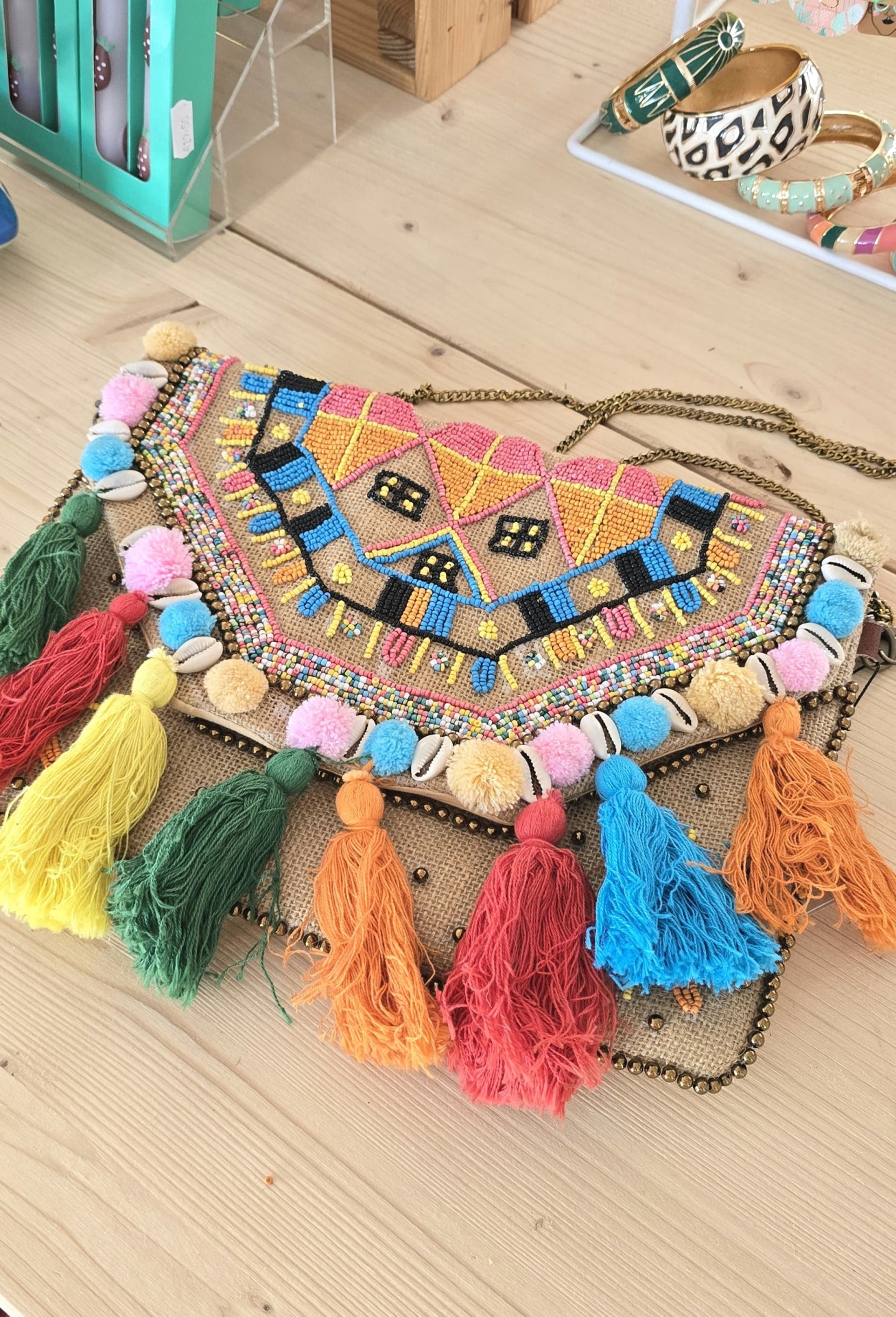 Bolsa colorida bordada com tasséis e conchas sobre superfície de madeira clara.
