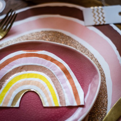 Conjunto de pratos decorados com arcos coloridos sobre superfície de madeira com talheres dourados