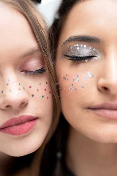 Close-up de dois rostos femininos com maquilhagem e confetes coloridos e prateados