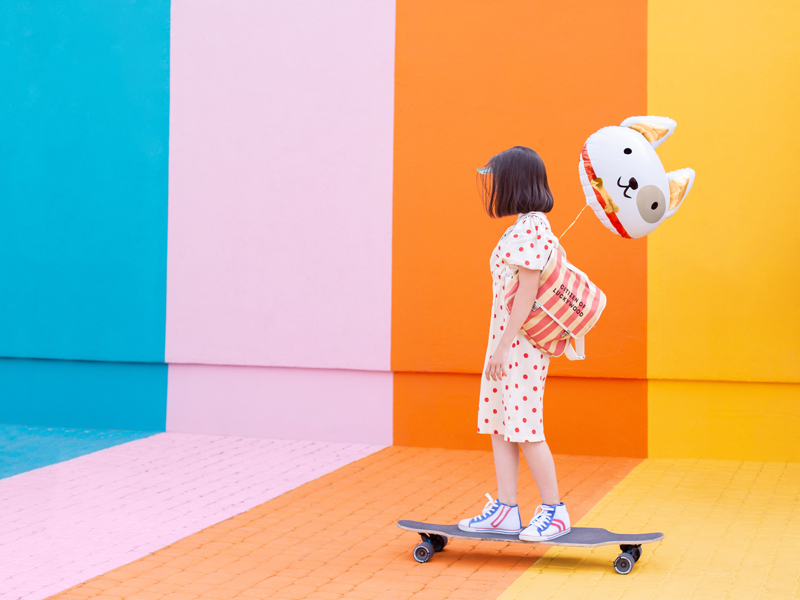 Criança de vestido com corações em skate em fundo colorido