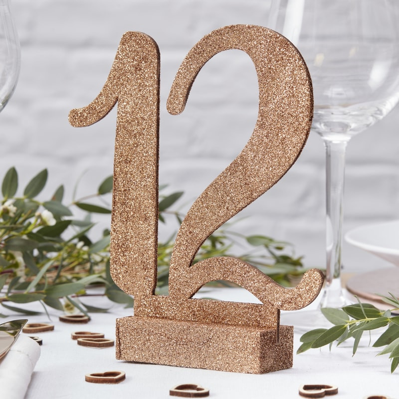 Número 12 de glitter dourado em base sobre mesa decorada com folhas e taças