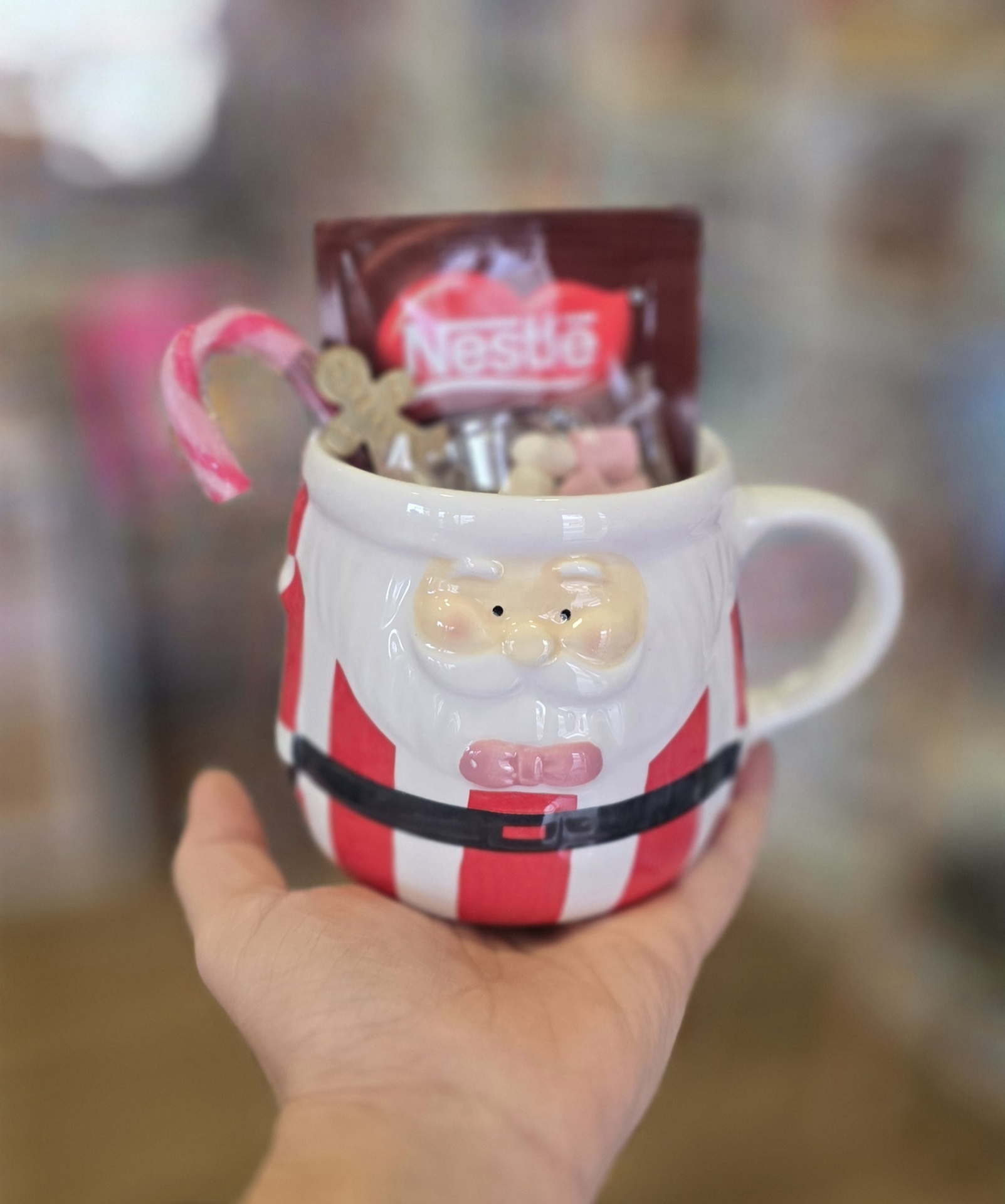 Caneca de Pai Natal com riscas vermelhas e brancas cheia de doces e pacote Nestlé