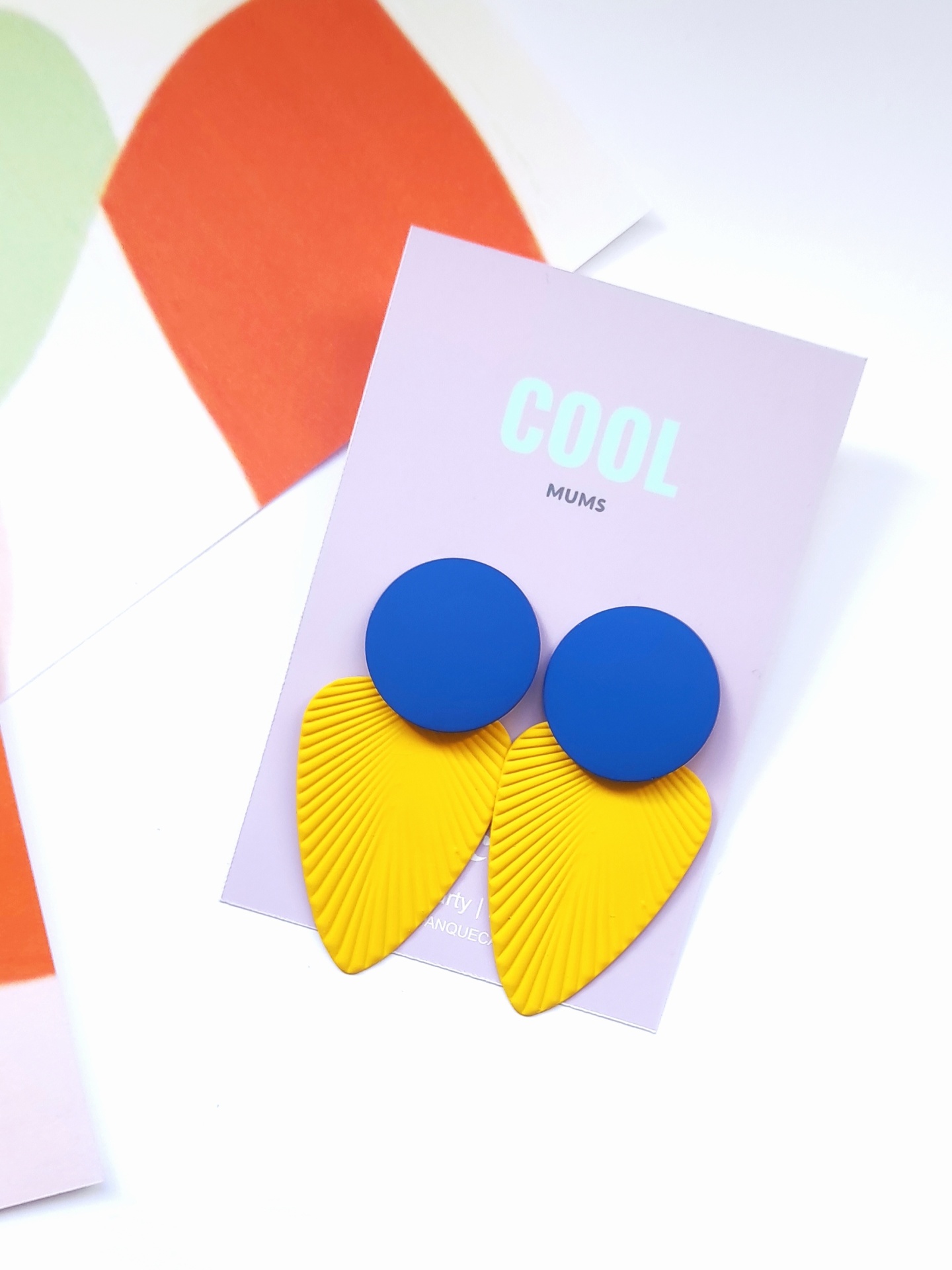 Brincos azul e amarelo em cartão lilás com texto COOL MUMS