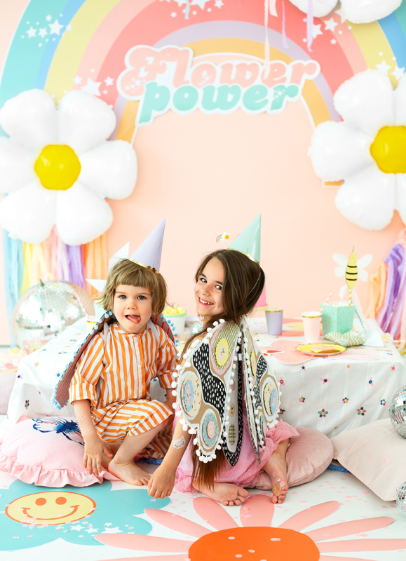 Crianças em festa infantil decorada com tema Flower Power, balões de flor e almofadas coloridas