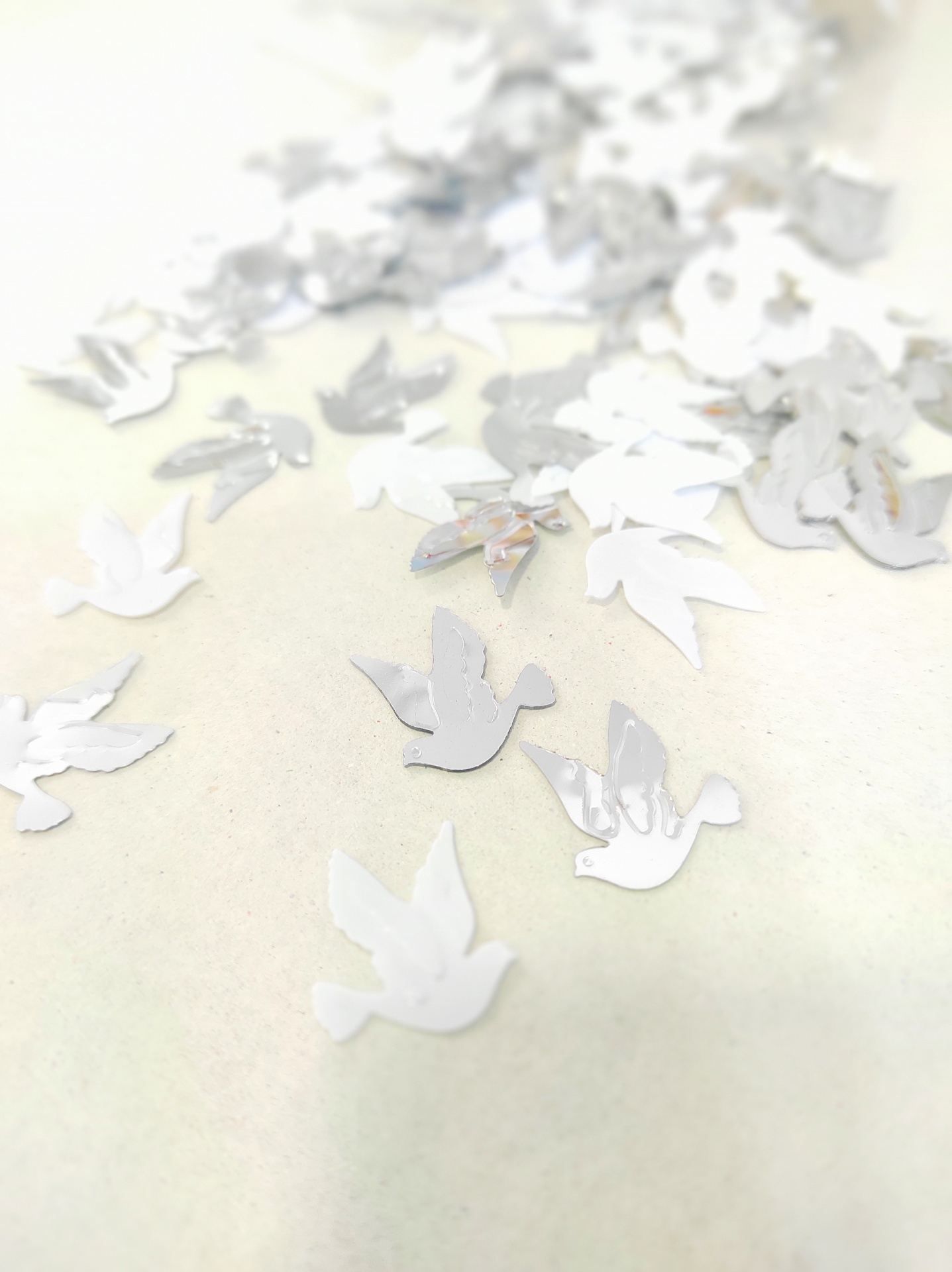 Confetes prateados em forma de pomba sobre superfície branca