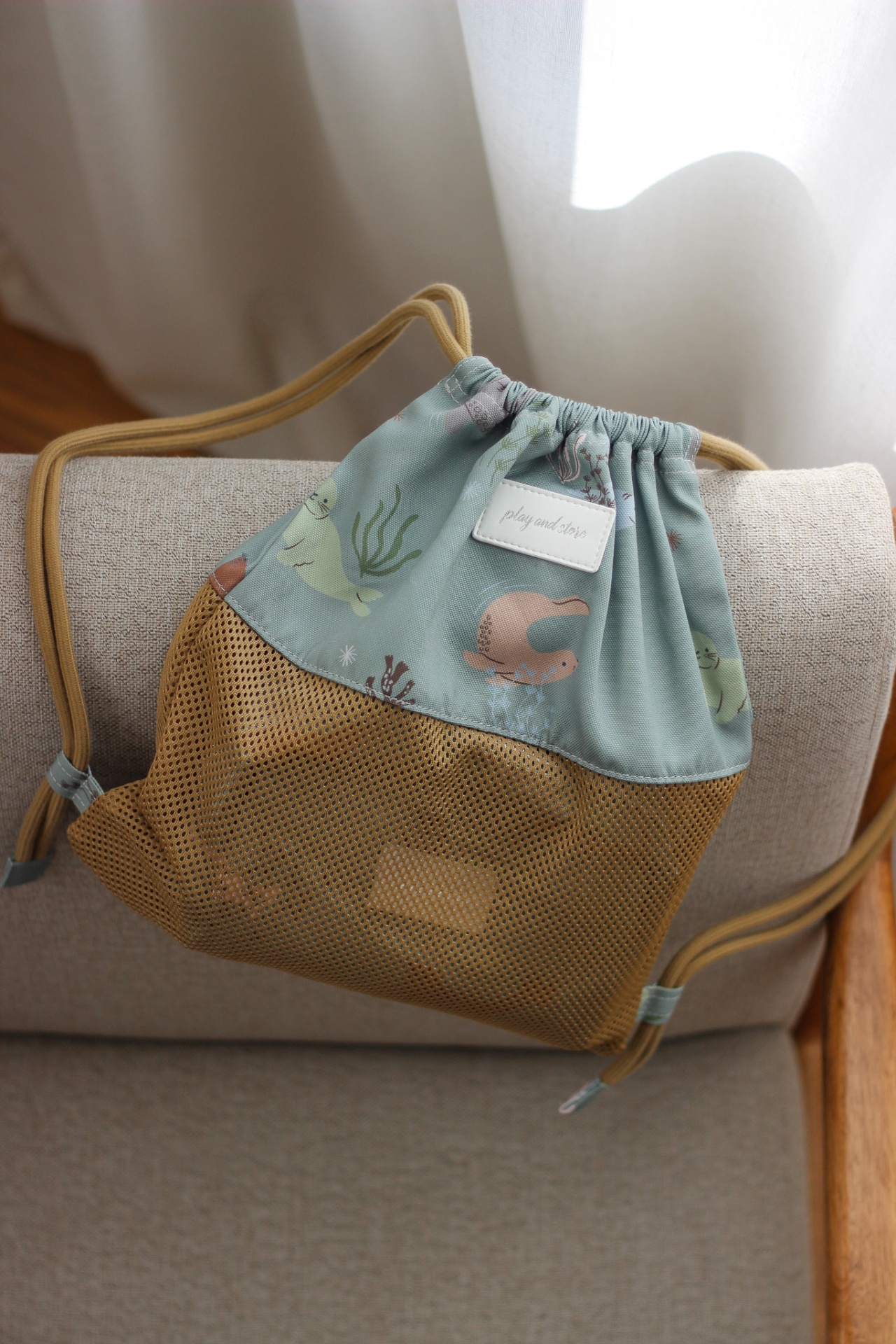 Mochila azul claro e amarela com padrão de animais marinhos em sofá cinza