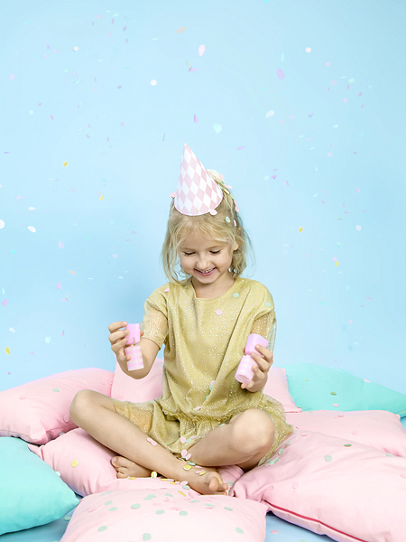 Criança com vestido dourado sentada em almofadas coloridas e chapéu de festa