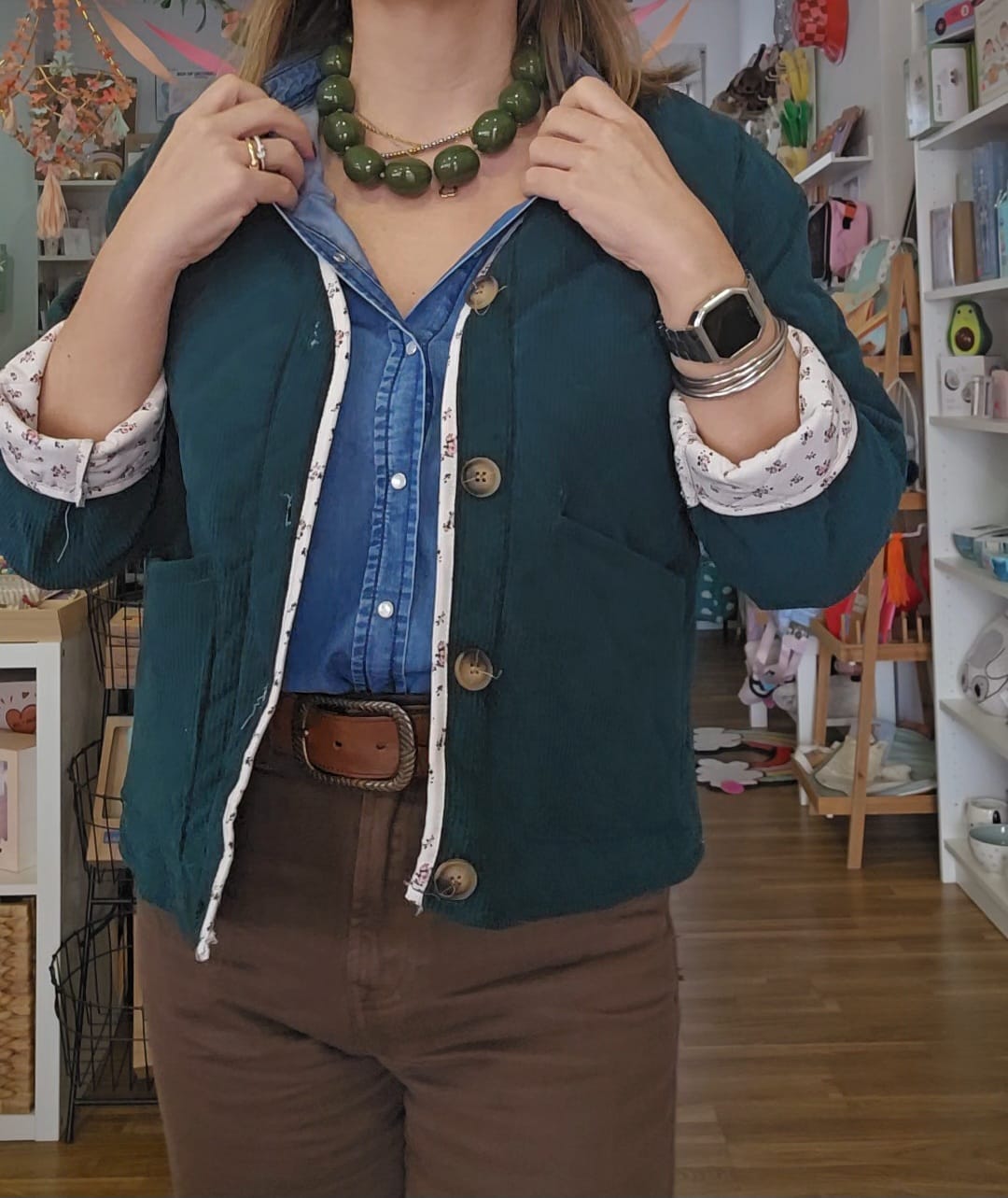 Casaco verde escuro com botões e forro floral sobre camisa azul e calças castanhas