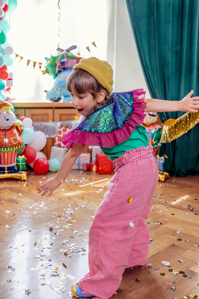 Criança com roupa colorida a brincar num chão com confetes e decoração de festa