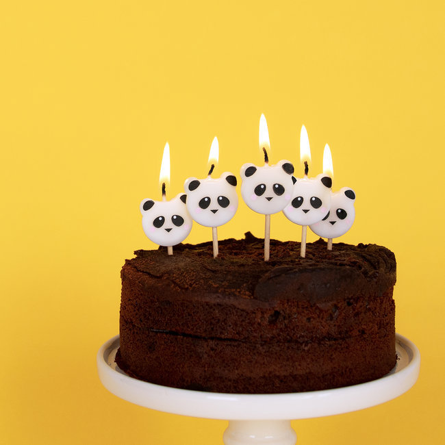 Bolo de chocolate com velas em forma de panda acesas sobre suporte branco, fundo amarelo