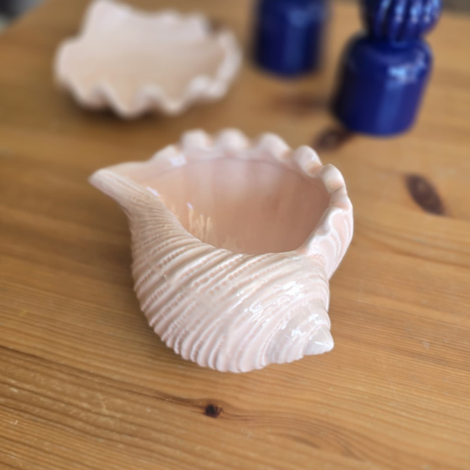 Taça decorativa em cerâmica rosa em forma de concha sobre mesa de madeira