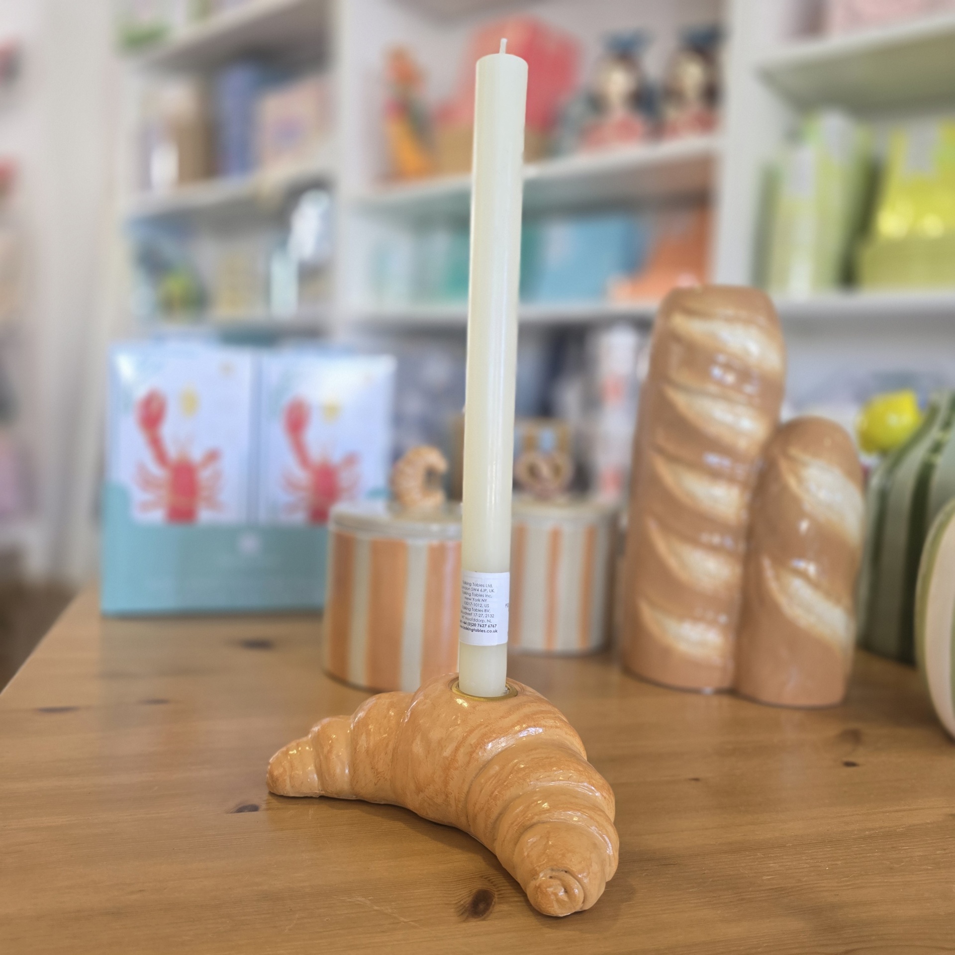 Suporte para vela em forma de croissant com vela branca sobre mesa de madeira.