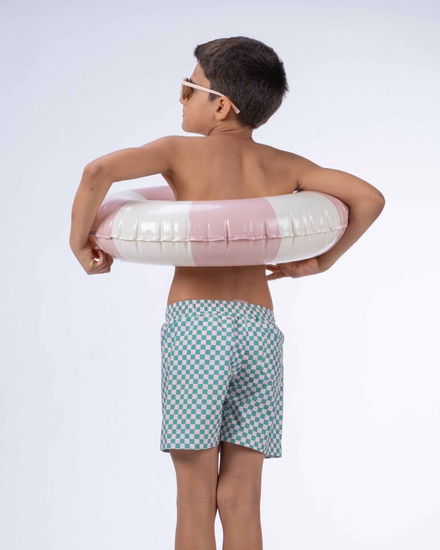Menino com boia insuflável e calção de banho xadrez.