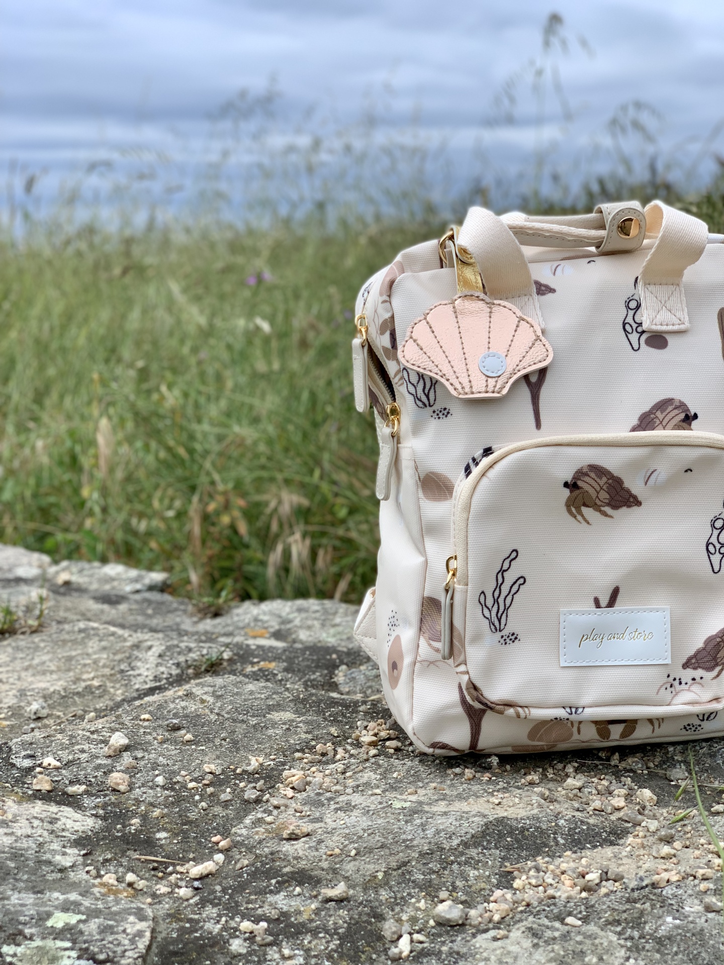 Mochila bege claro com padrão marinho e pendente de concha em rocha ao ar livre