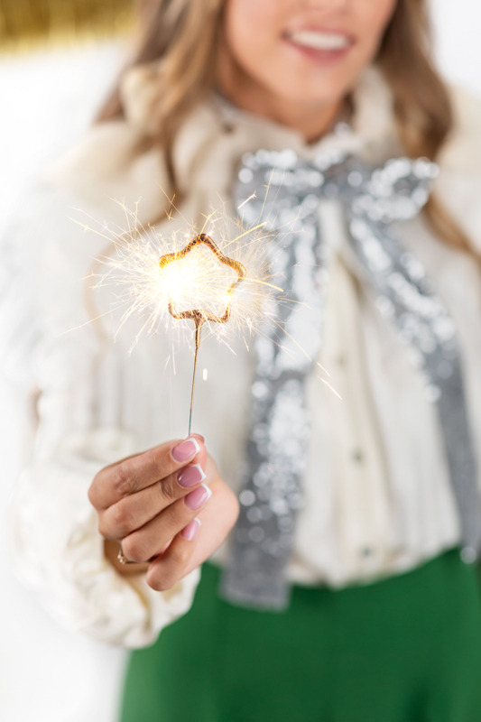 Pessoa segura faísca em forma de estrela acesa com blusa branca e laço prateado