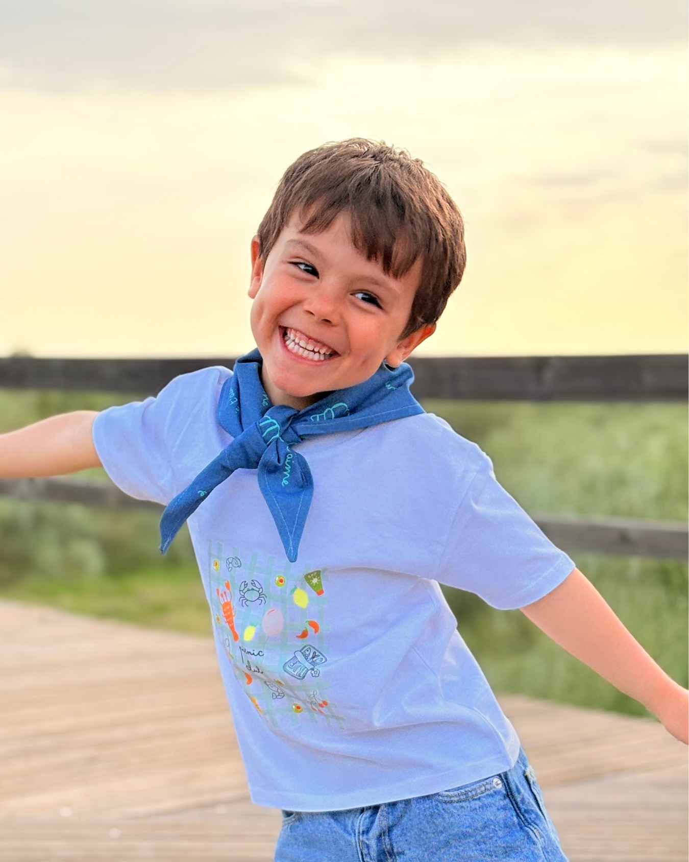 Criança sorridente com t-shirt branca e lenço azul ao pescoço ao ar livre