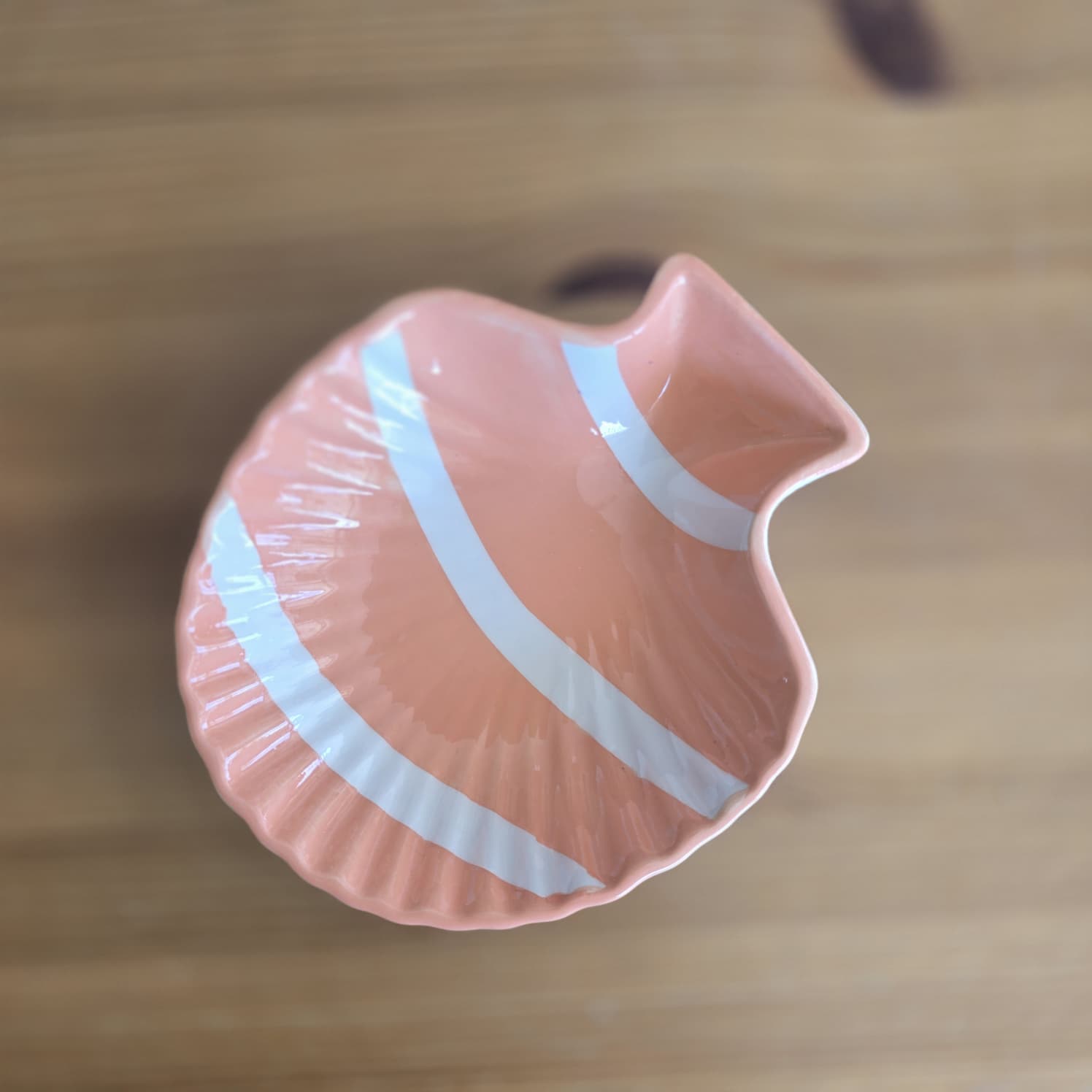 Prato de cerâmica em formato de concha rosa salmão com riscas brancas.