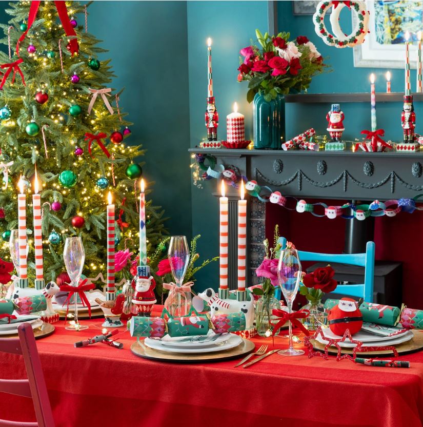 Mesa de jantar natalícia com velas às riscas, rosas, bonecos de madeira e árvore de Natal iluminada