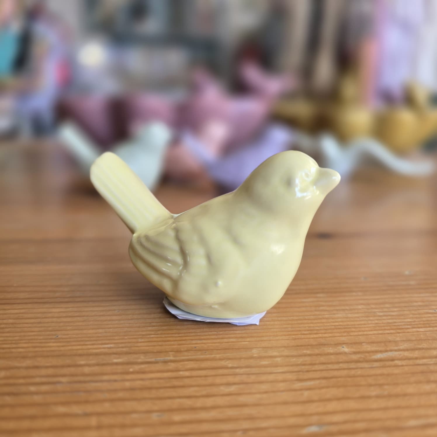 Figurinha de pássaro amarelo de cerâmica sobre mesa de madeira