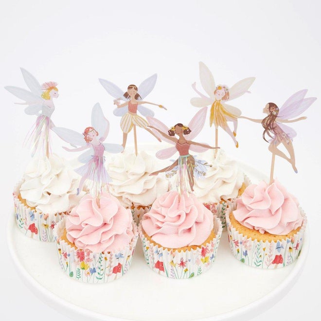 Cupcakes com creme branco e rosa e toppers de fadas em papel num prato branco