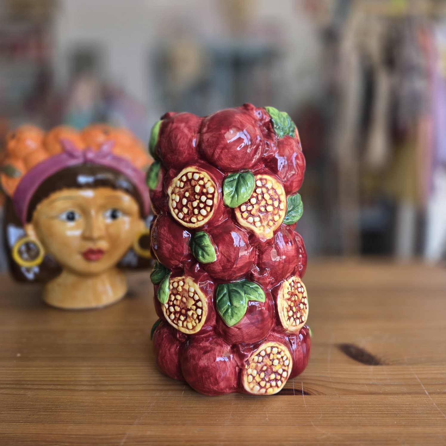 Vaso cerâmico decorativo com padrão de romãs e jarro com rosto feminino ao fundo