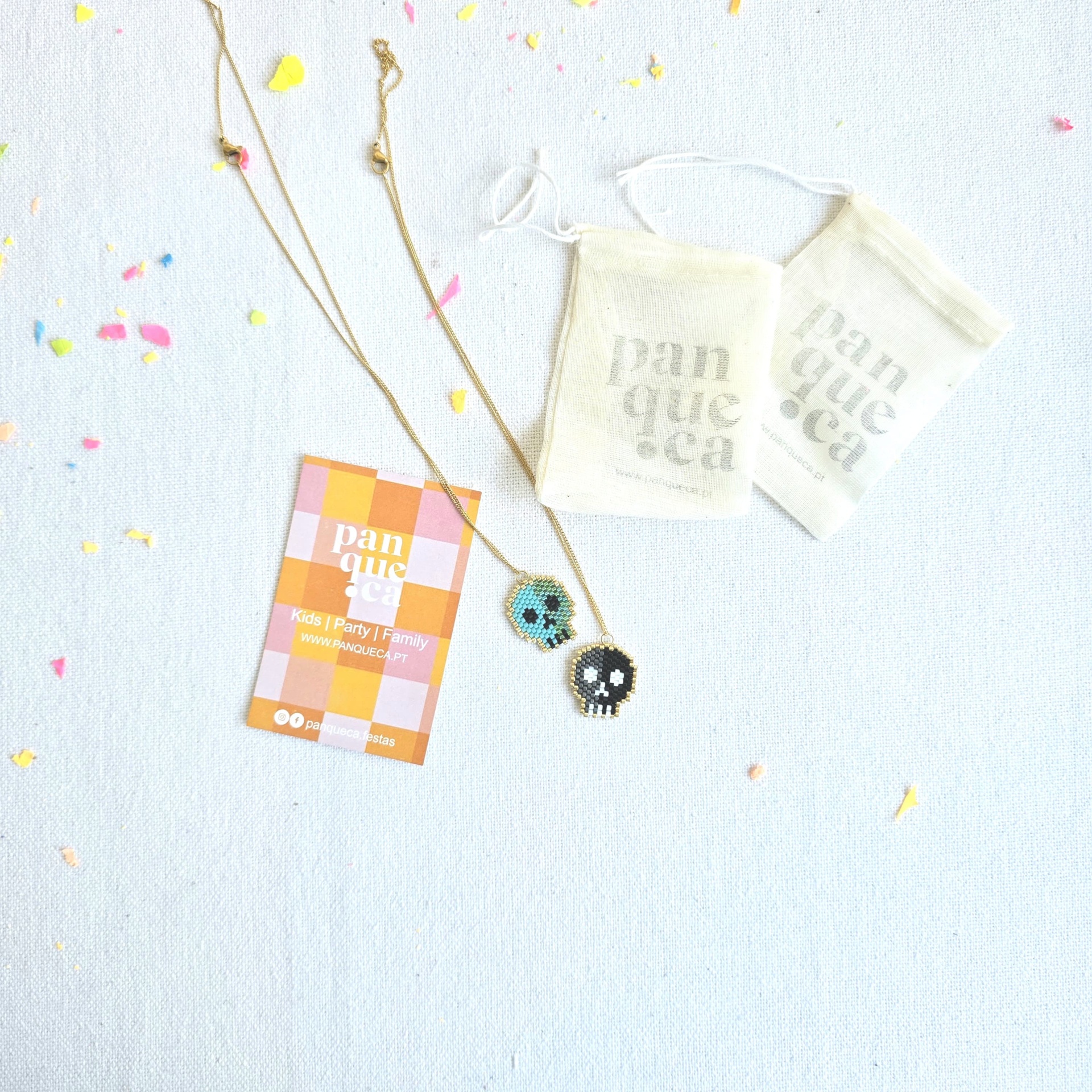 Dois colares com pendentes de caveira bordada e sacos de tecido com texto panqueça