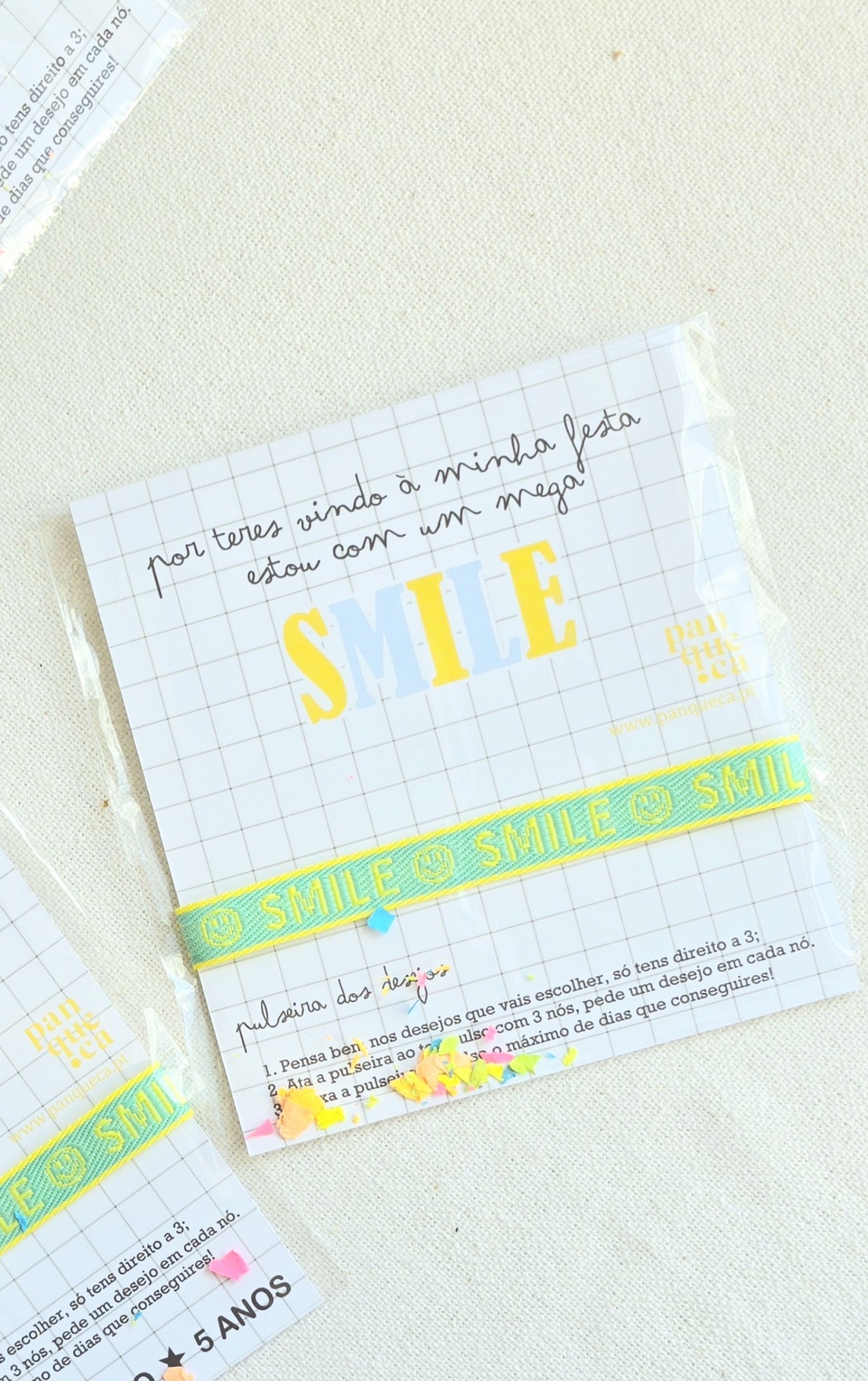 Pulseira azul claro com texto SMILE amarela em embalagem branca com padrão quadriculado