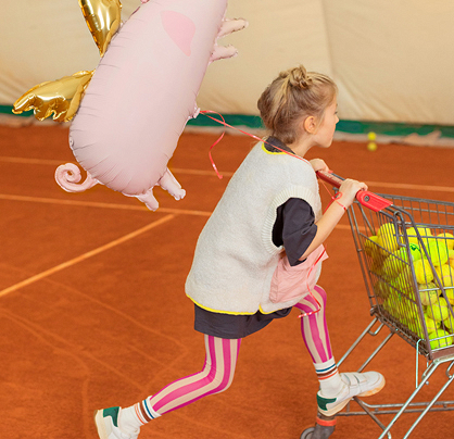 Menina empurrando carrinho com bolas de ténis e balão de porquinho