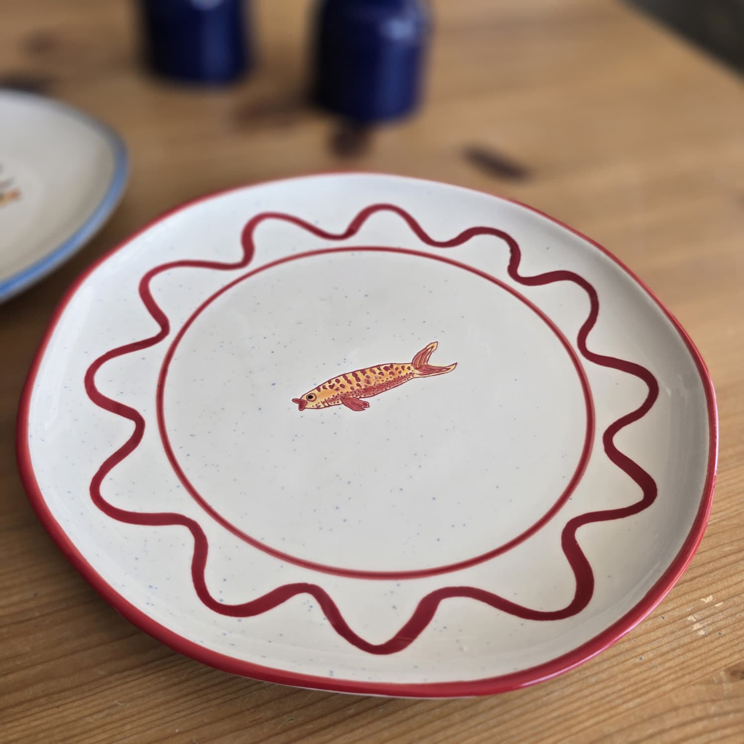 Prato branco com borda e padrões vermelhos e desenho de peixe no centro