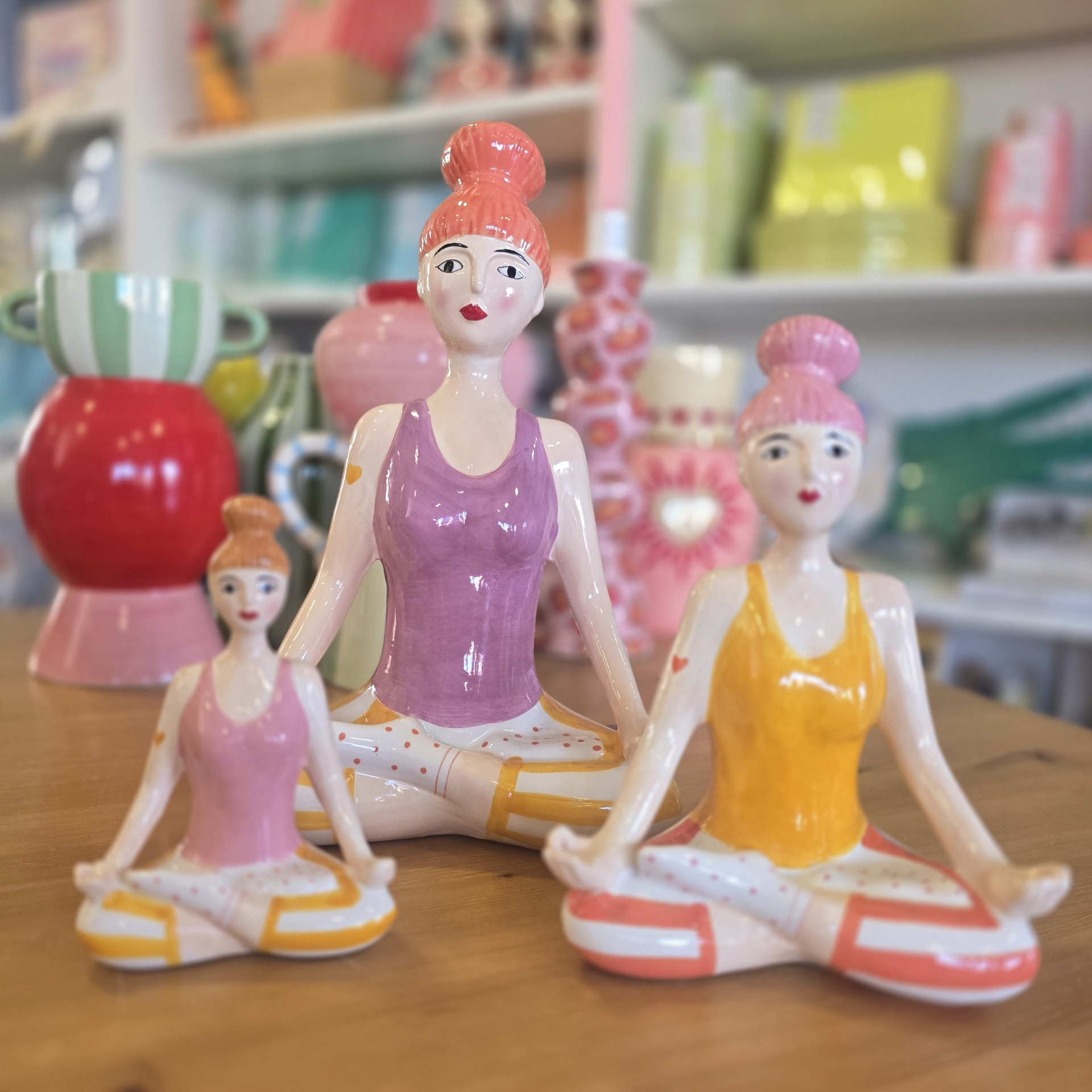 Três estatuetas cerâmicas coloridas em pose de meditação.